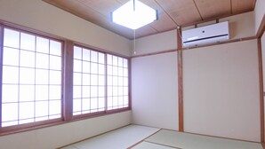 Une pièce dont le sol est recouvert de tatamis, avec une grande fenêtre à carreaux et un luminaire au plafond.