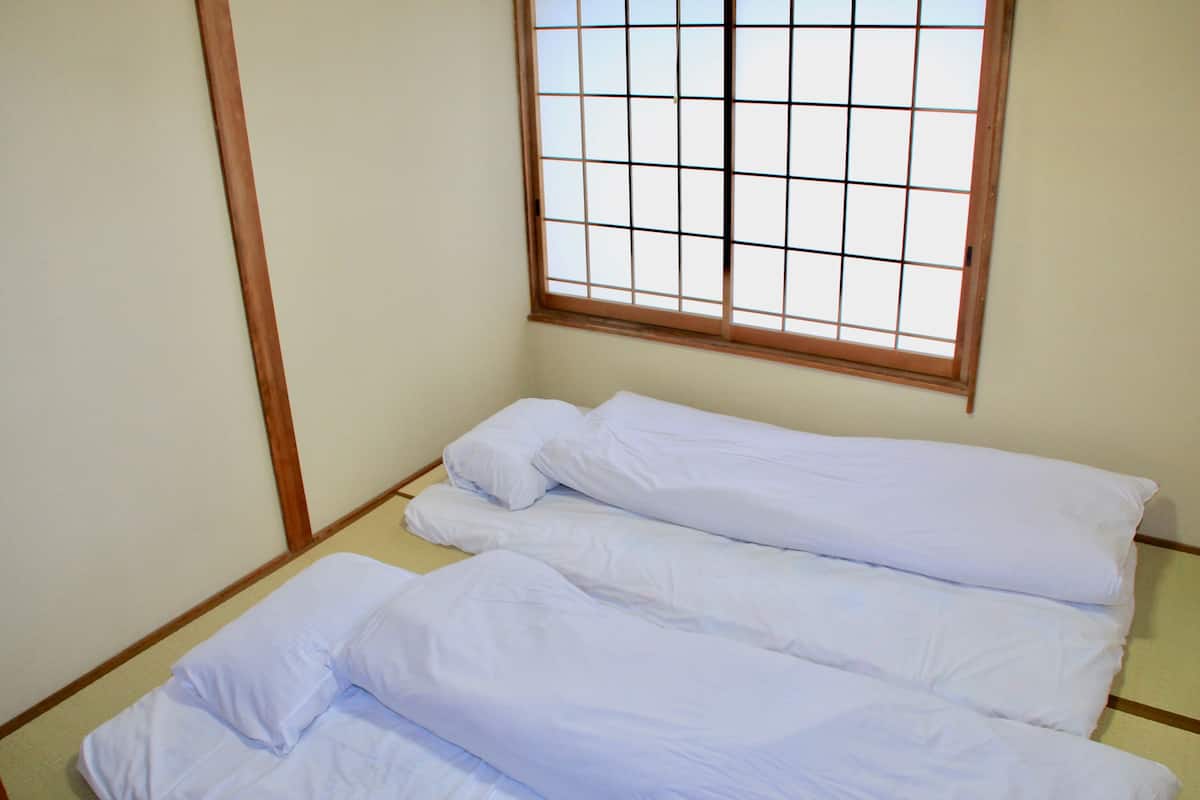 A room with a bed, a window with a grid pattern, and wooden wall trim.