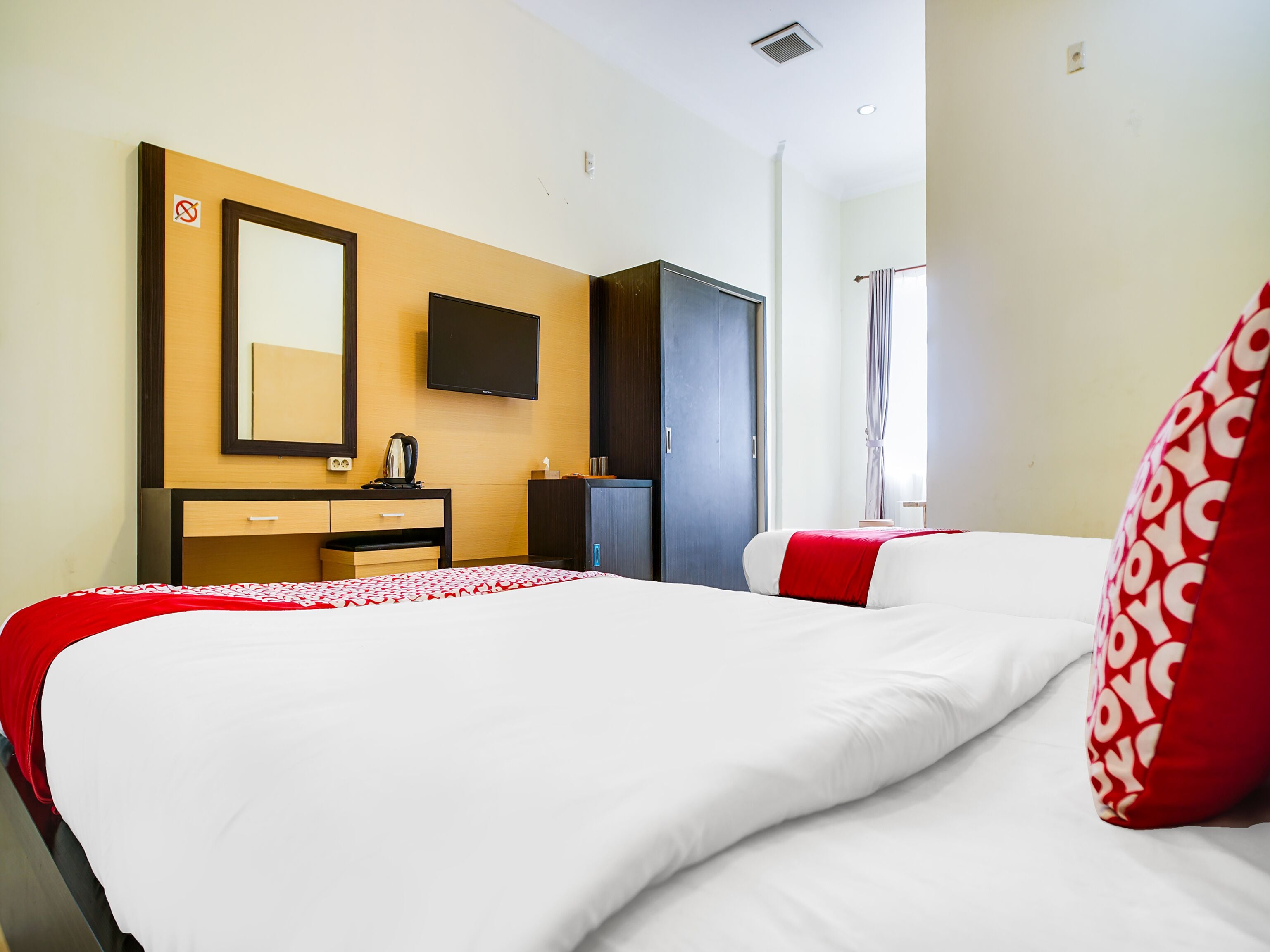 A hotel room with a bed, a dresser, a TV, and a window with curtains.