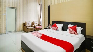 Ein Hotelzimmer mit einem großen Bett, zwei Sesseln, einem Nachttisch und einer Tür.