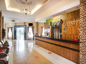 Een hotel receptie met een houten balie, een kroonluchter en een zithoek met stoelen.