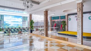 Eine geräumige Lobby mit Schachbrettmuster-Bodenbelag, einer Kristallleuchtreiter und einer Sitzecke mit roten Stühlen, sowie einem großen Fenster mit Blick auf Grünflächen.