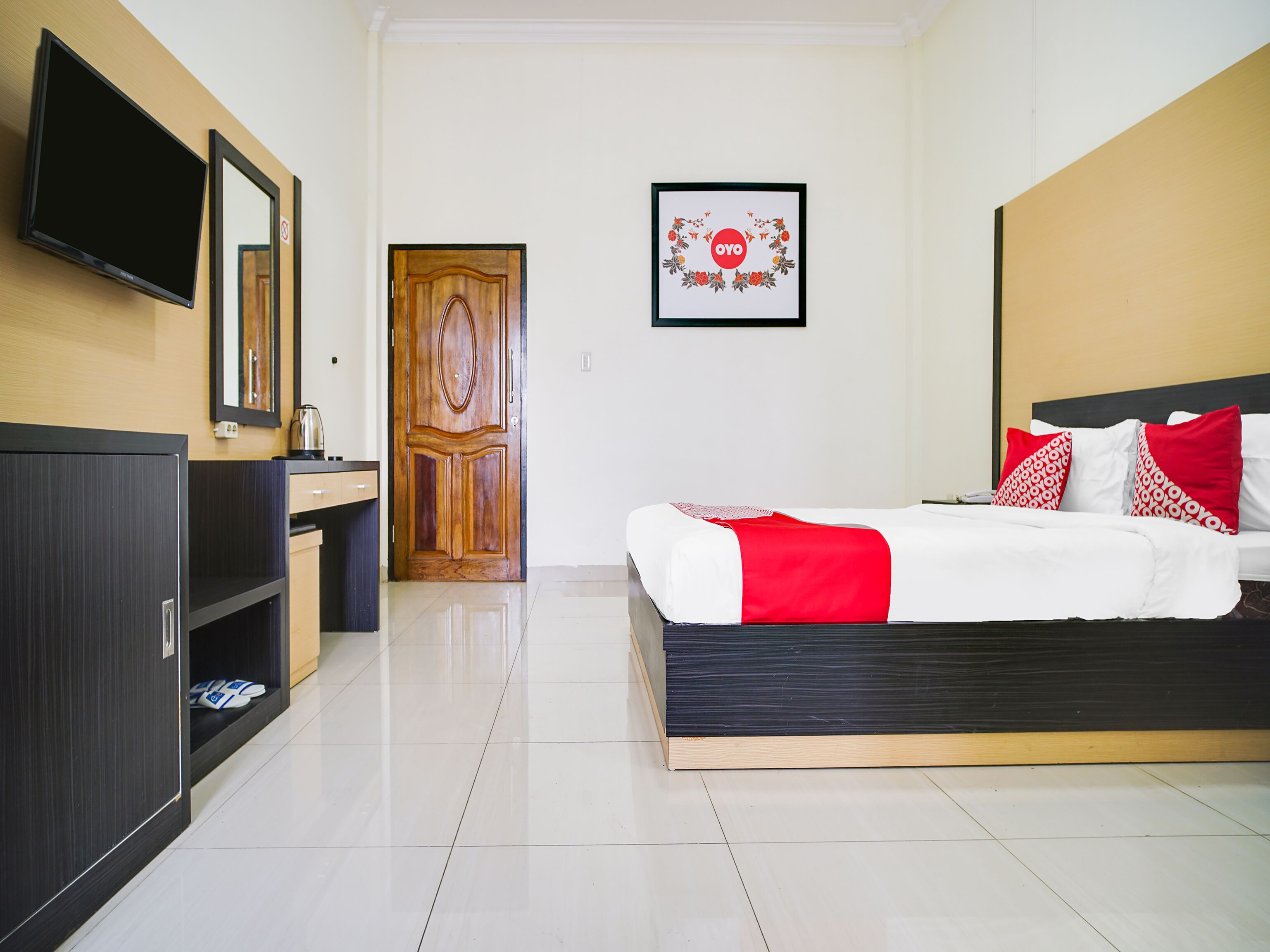 A hotel room with a bed, a TV, a wooden door, and a framed picture on the wall.
