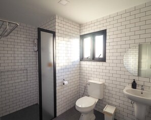 A bathroom with white subway tiles, a toilet, a sink, a mirror, and a shower area. - WIW Minihotel (Bangkok)