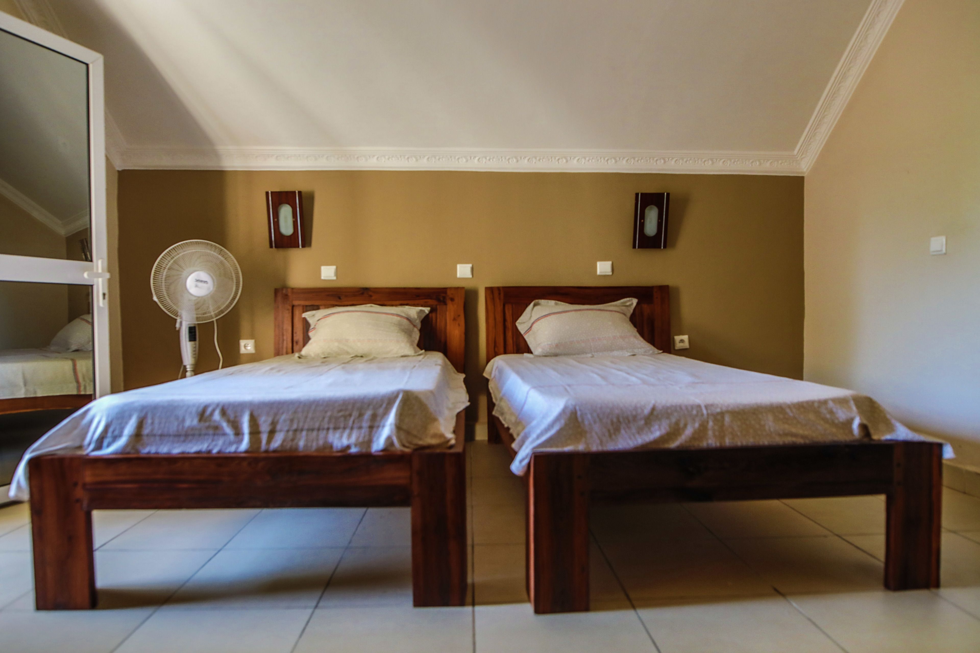 A room with two wooden beds, a standing fan, and a mirror on the left wall.