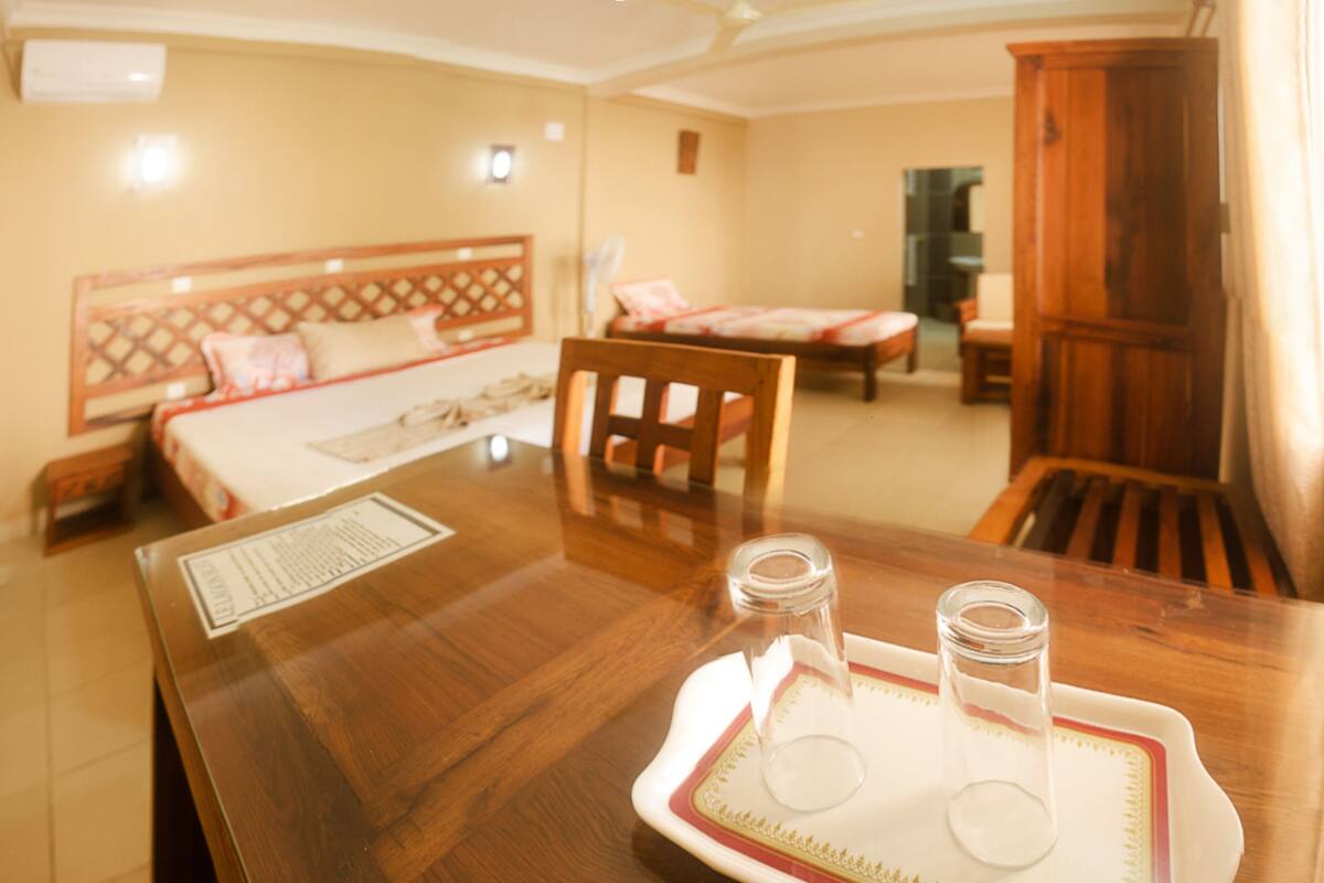 A hotel room with a wooden dining table, a bed with a headboard, and a wardrobe.