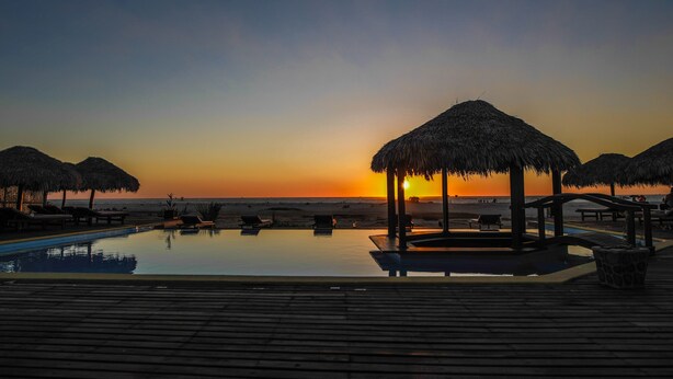 A sunset view from an infinity pool with thatched umbrellas and lounge chairs. - Laguna Beach (Morondava)