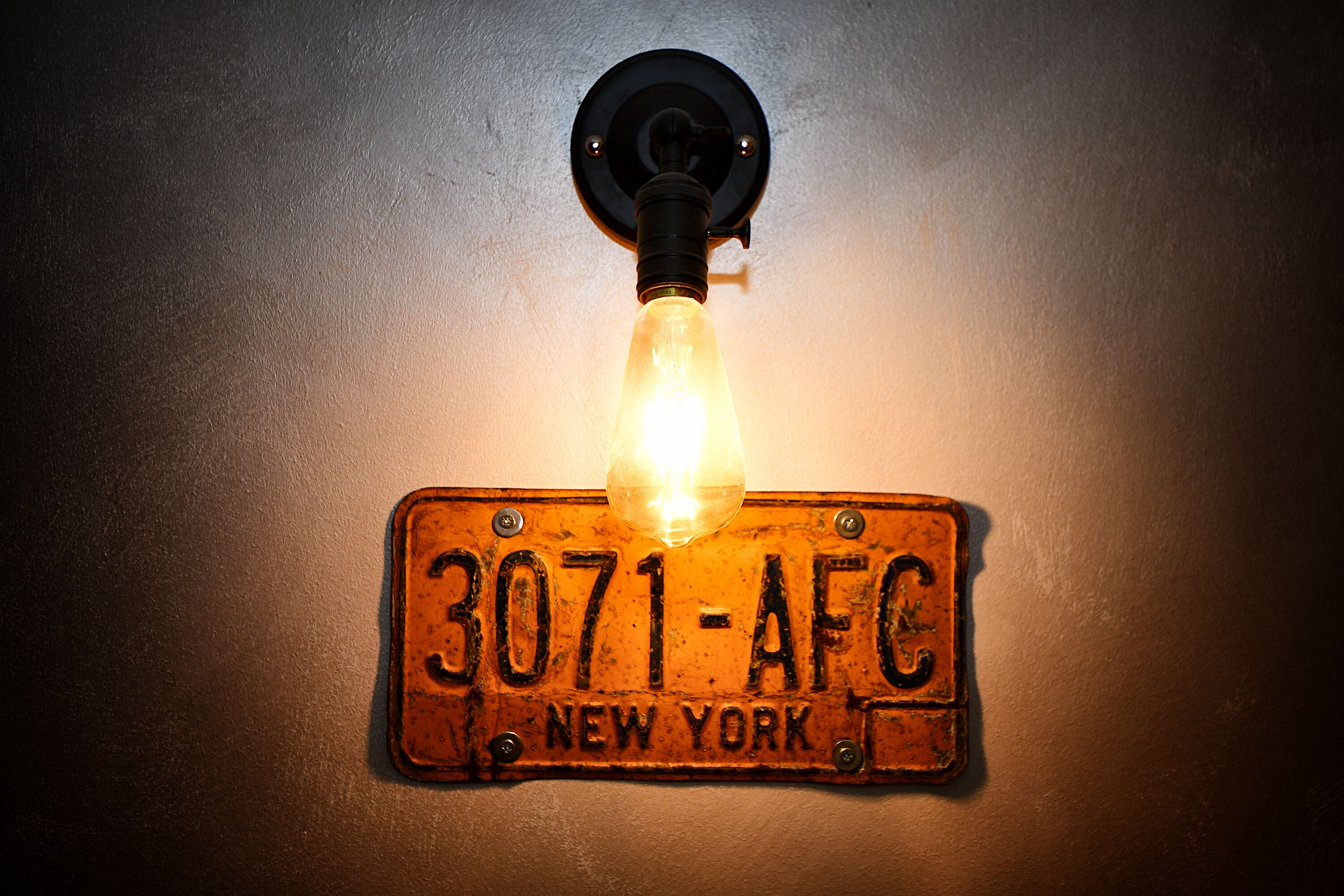 Luminária fixada na parede com placa de carro estilo vintage com a inscrição "3071-AFC NEW YORK".