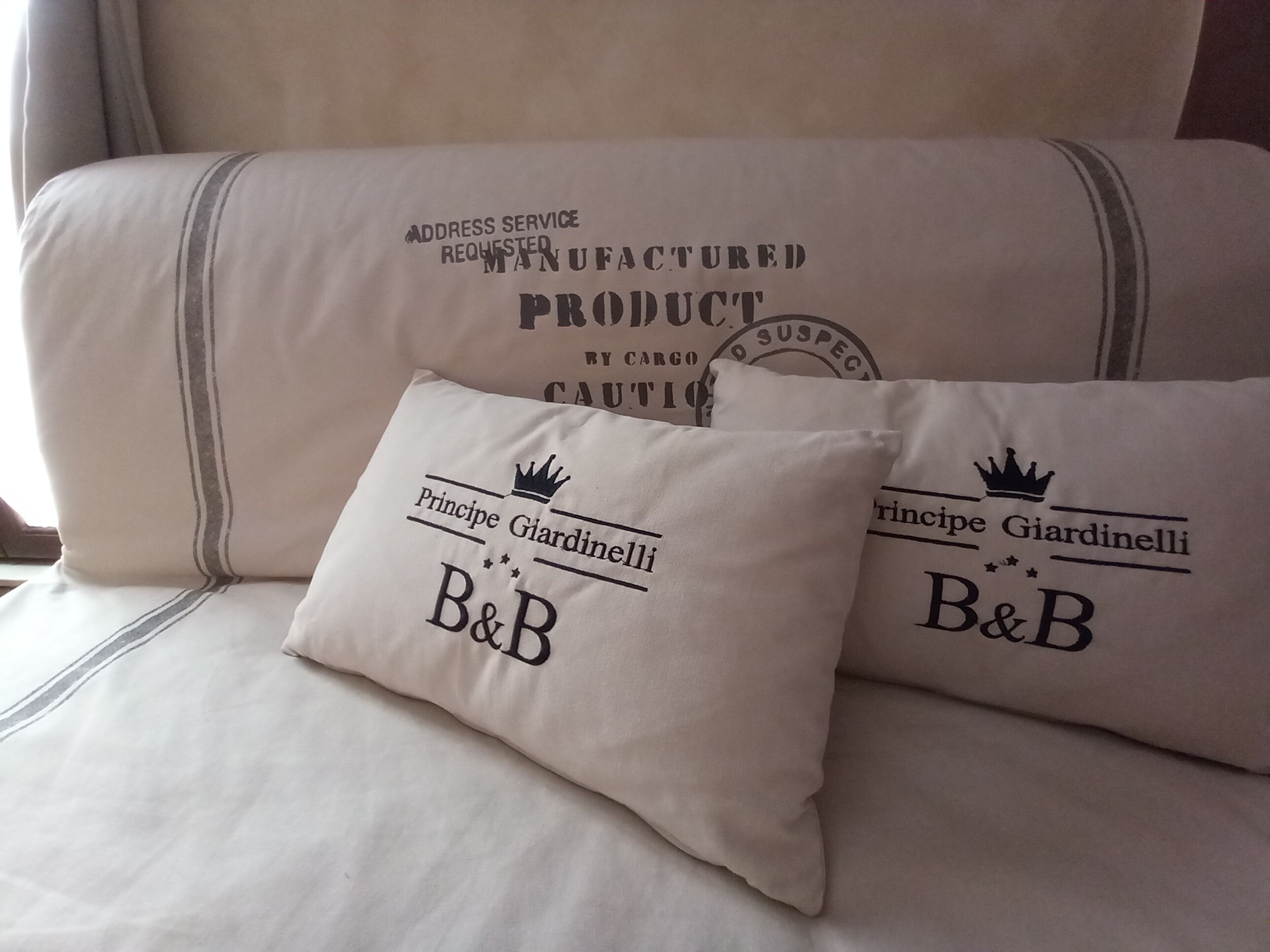 Una cama con un almohadón y una colcha. El almohadón tiene texto y el logotipo de una corona.