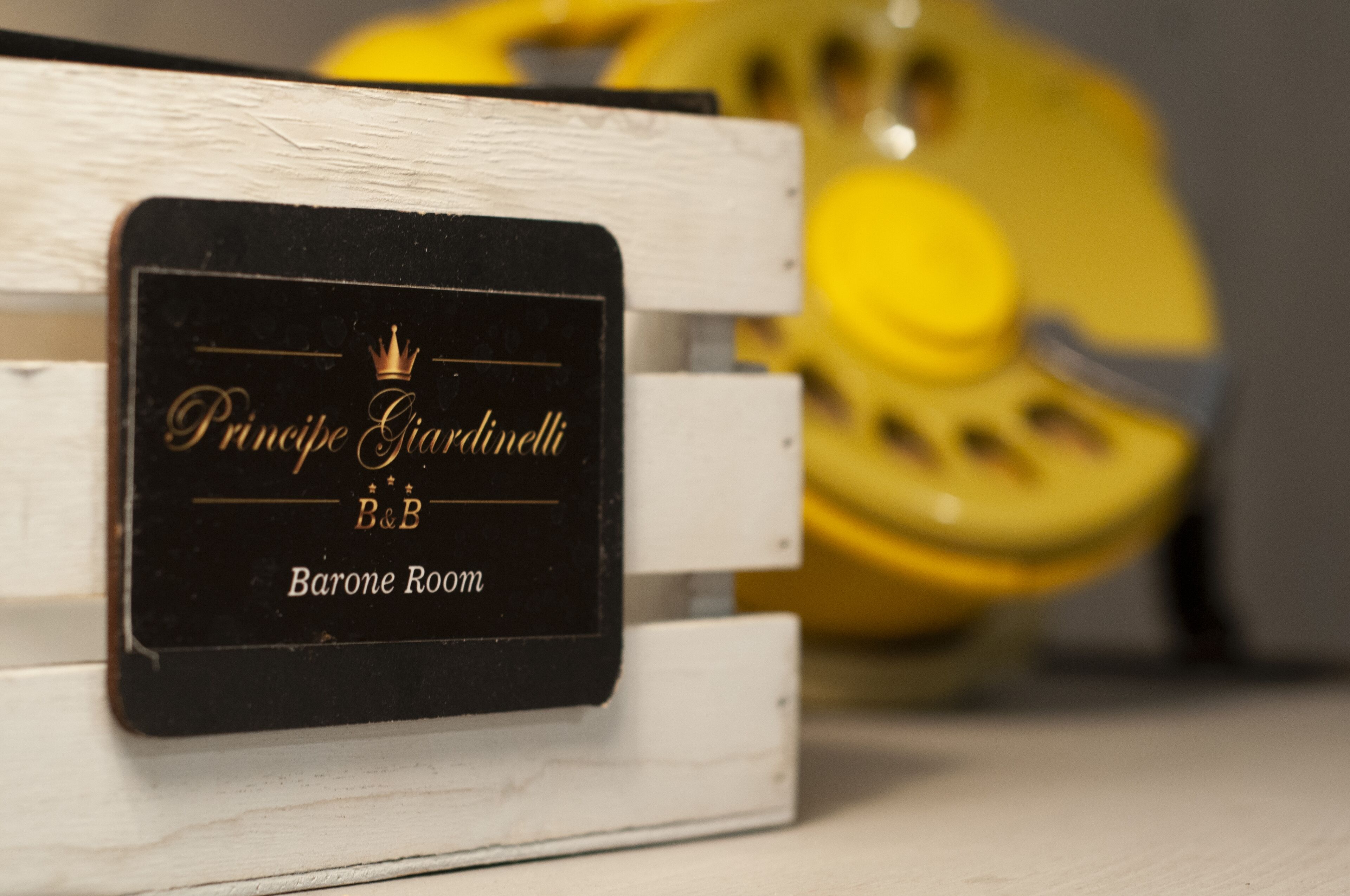 Un letrero negro con letras doradas sobre una superficie de madera blanca, que indica "Príncipe Giacinto B&B Barone Room".