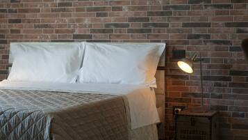 A bed with white linens and a quilted cover, a bedside lamp, and a brick wall.