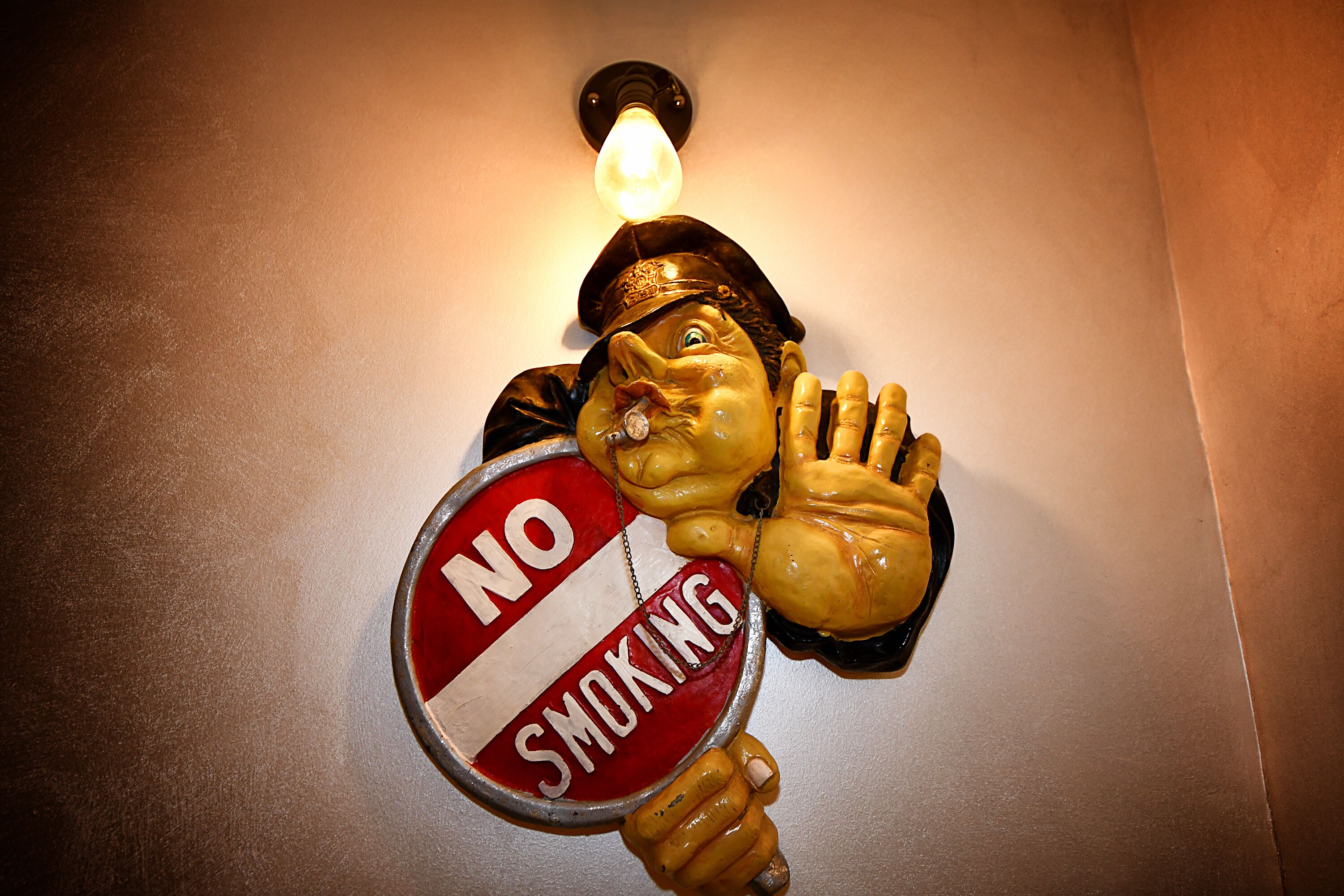 A wall-mounted sculpture of a man holding a 'No Smoking' sign.