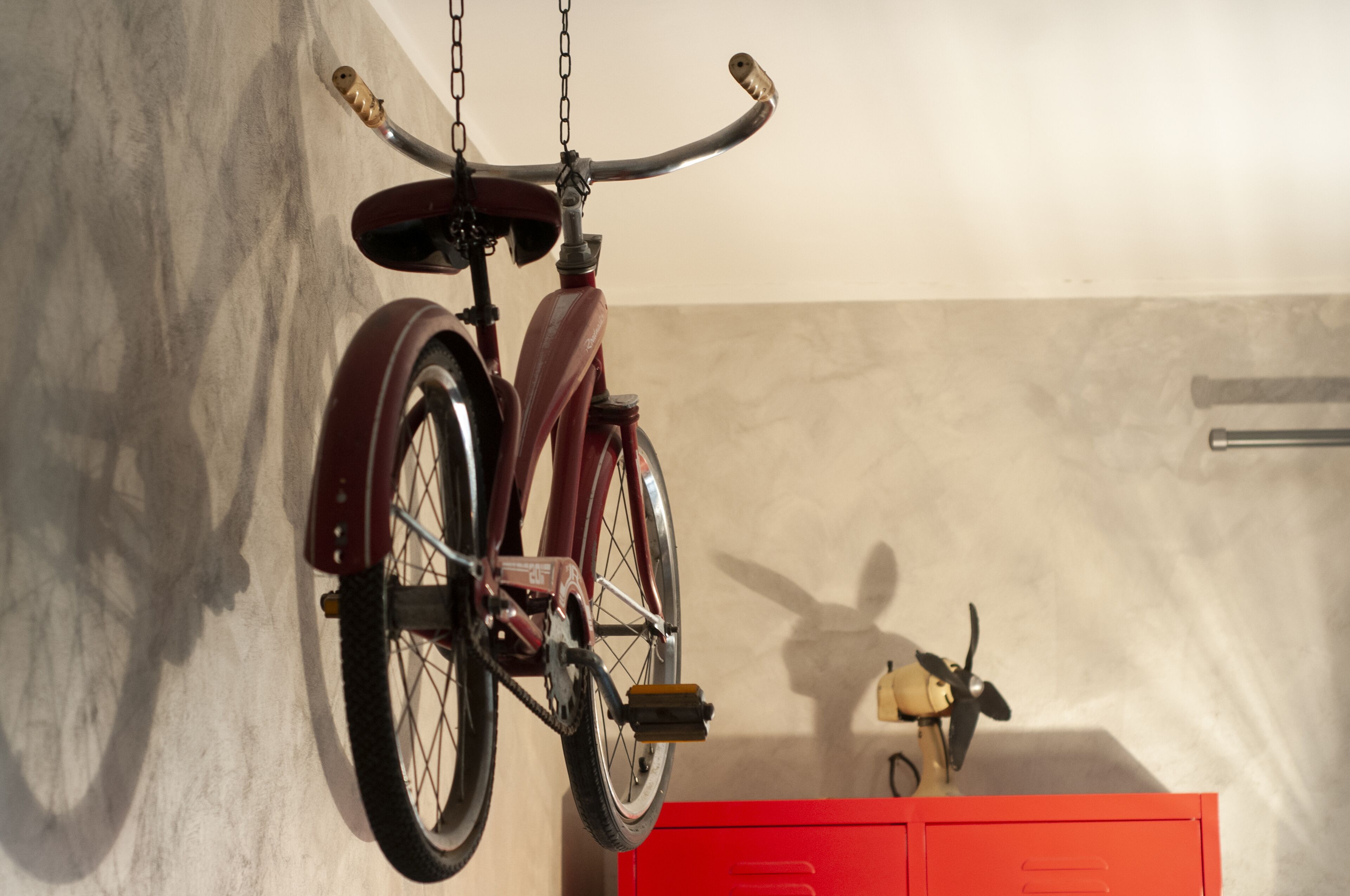 Un vélo est accroché au mur, et en dessous se trouve un meuble rouge.