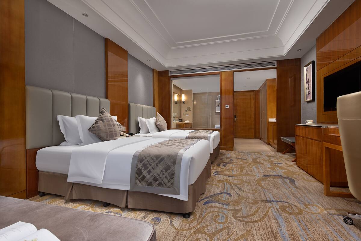 A hotel room with two beds, a desk, and a TV.