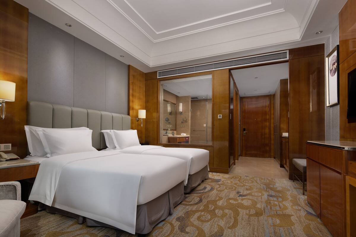 A hotel room with two beds, a desk with a phone, a TV, and a bathroom visible through an open door.