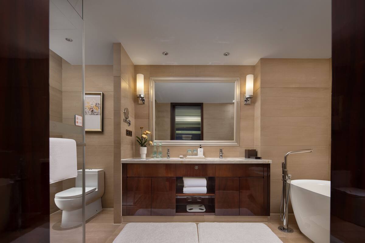 A modern bathroom with a glass shower enclosure, a freestanding bathtub, and a vanity with a large mirror and wall-mounted lights.