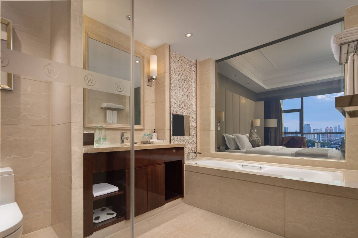 A modern bathroom with a large mirror, a bathtub, and a city view.