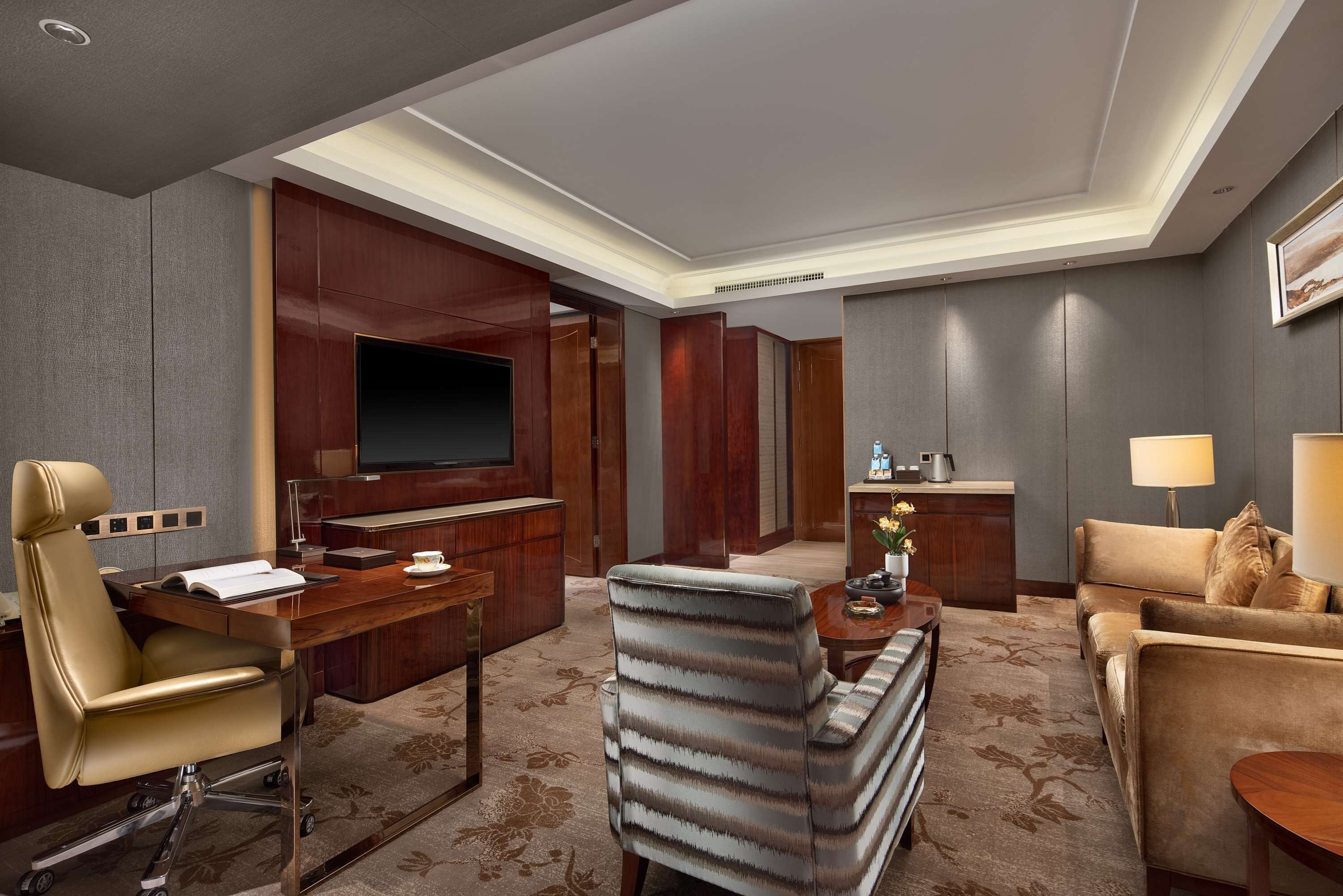 A hotel room with a desk, a sofa, a TV, and a kitchenette.