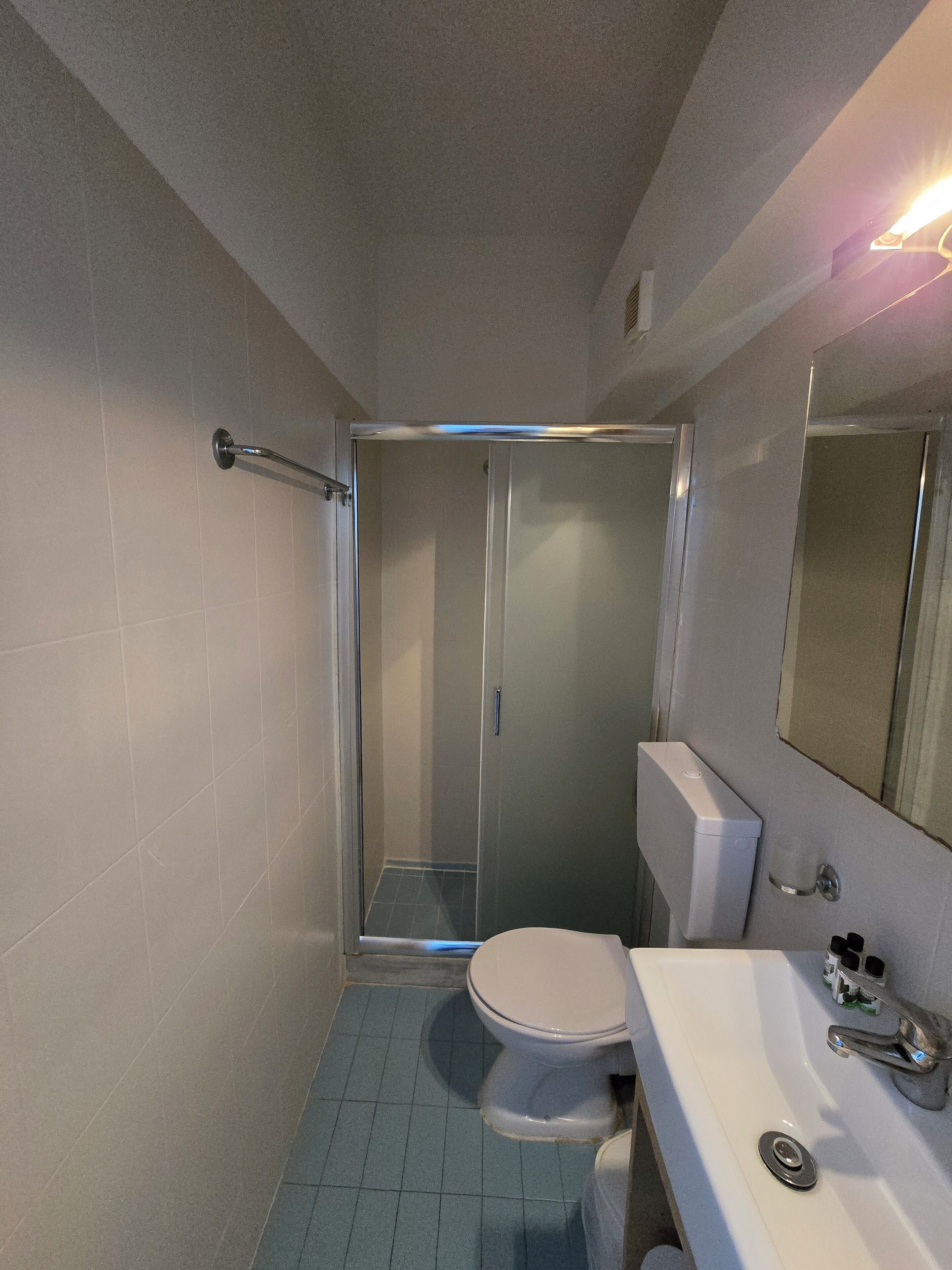 A bathroom with a shower, toilet, sink, and mirror.