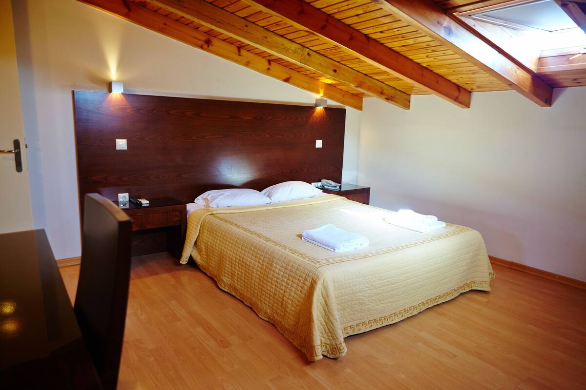 Una camera da letto con una testiera in legno, un letto con copriletto giallo, due comodini e un tavolino da notte.