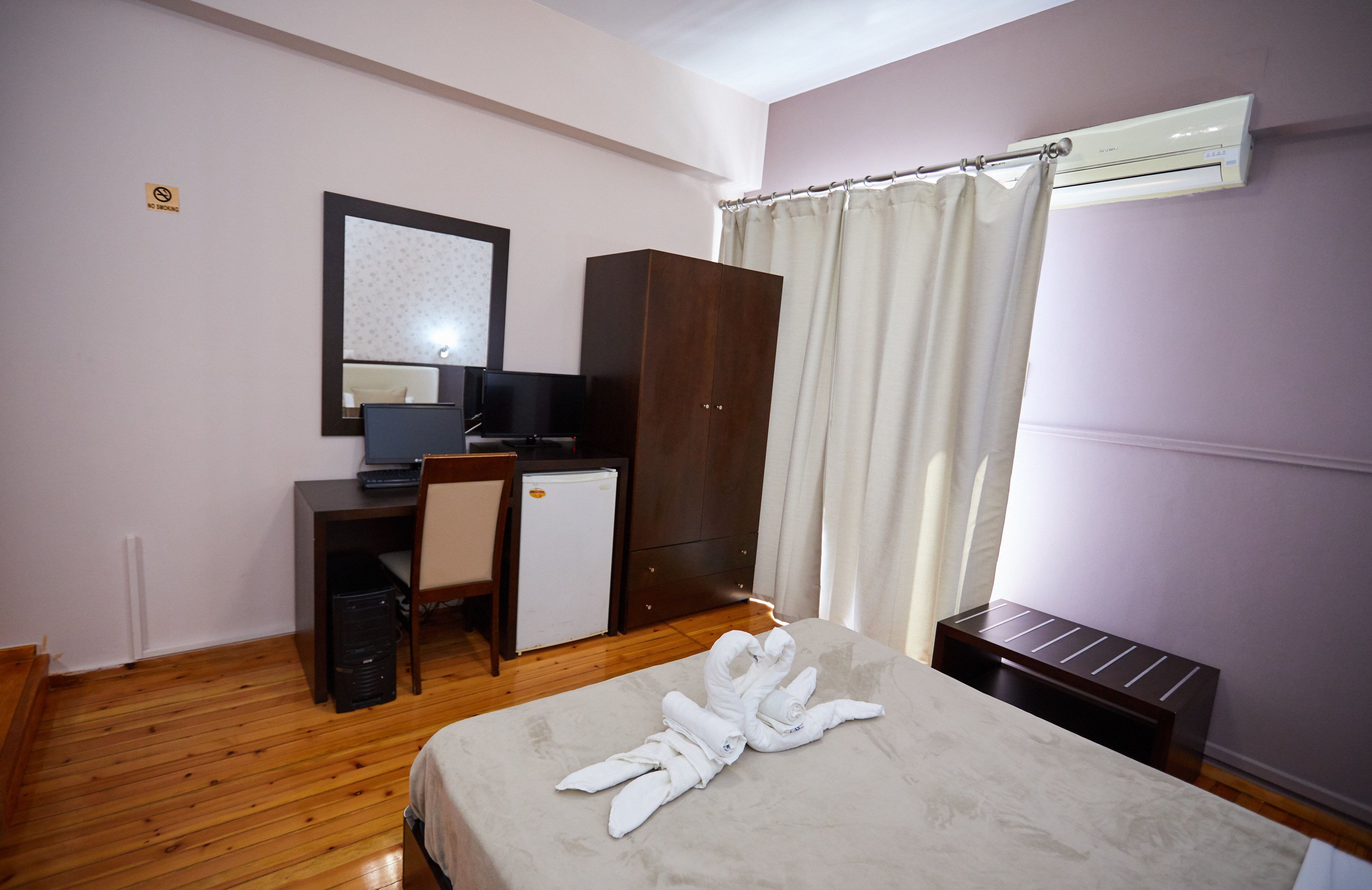 A hotel room with a bed, a desk with a computer, a small refrigerator, a wardrobe, and a shower curtain.
