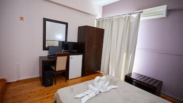 A hotel room with a bed, a desk with a computer, a small refrigerator, a wardrobe, and a shower curtain.