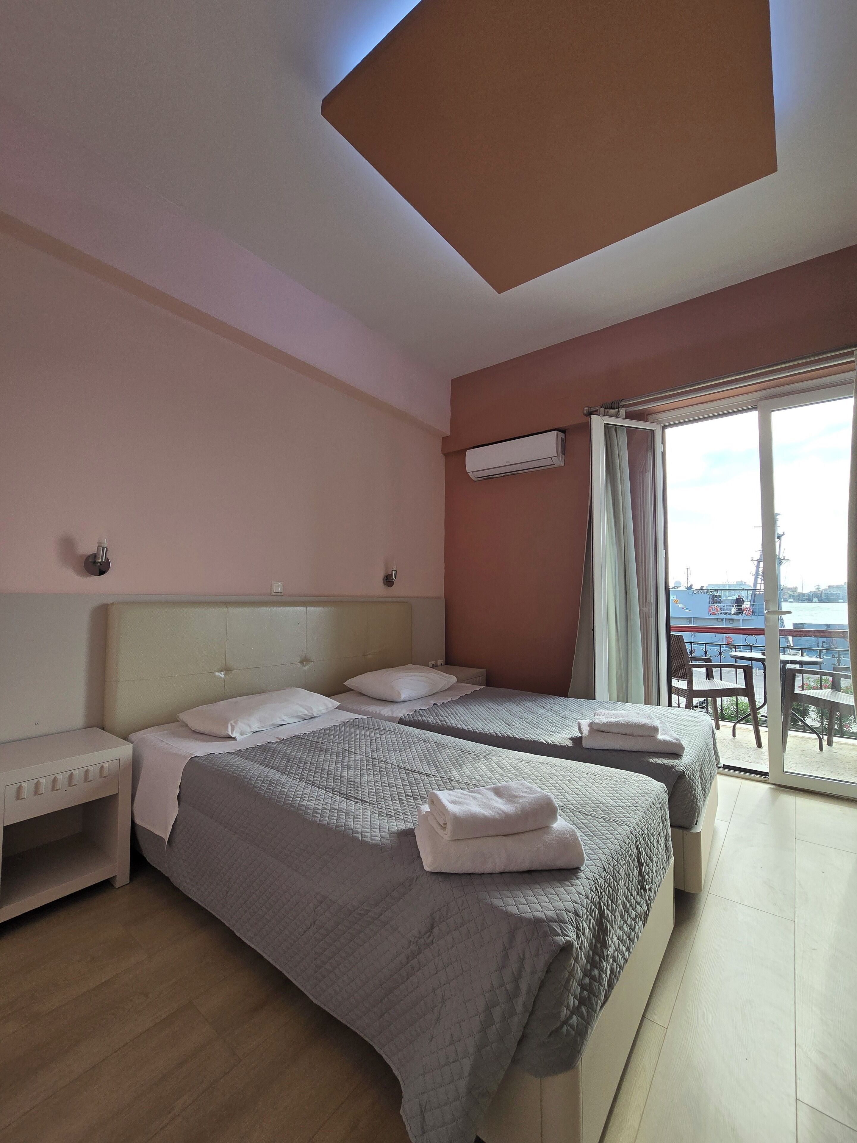 Een hotelkamer met twee bedden, een nachtkastje, een raam met uitzicht op zee, en een airconditioning.