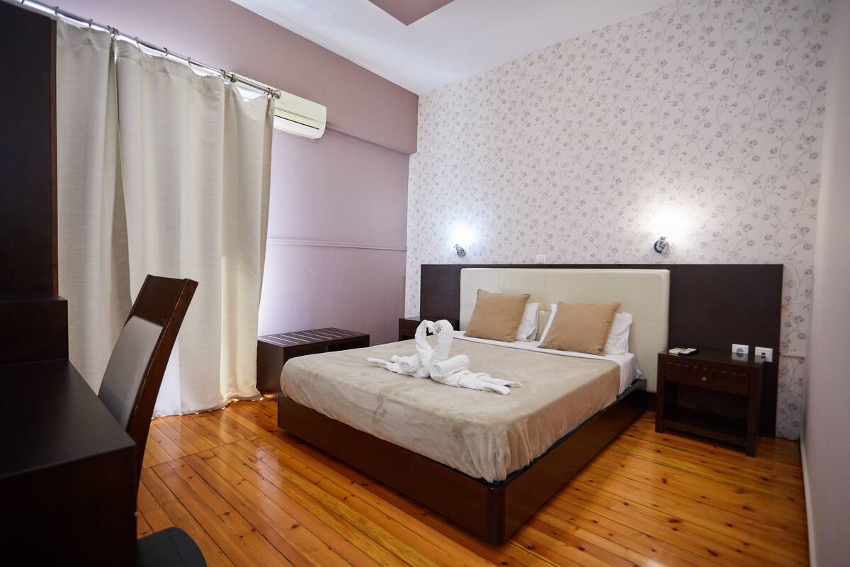 Un letto rifatto con cura, un'accogliente disposizione di asciugamani, un pavimento in legno, una scrivania con sedia e un comodino con lampada.