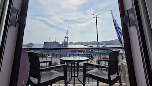 A balcony with two chairs and a table, overlooking a harbor with ships and a flag. - Aegean Sea Rooms (Chios)