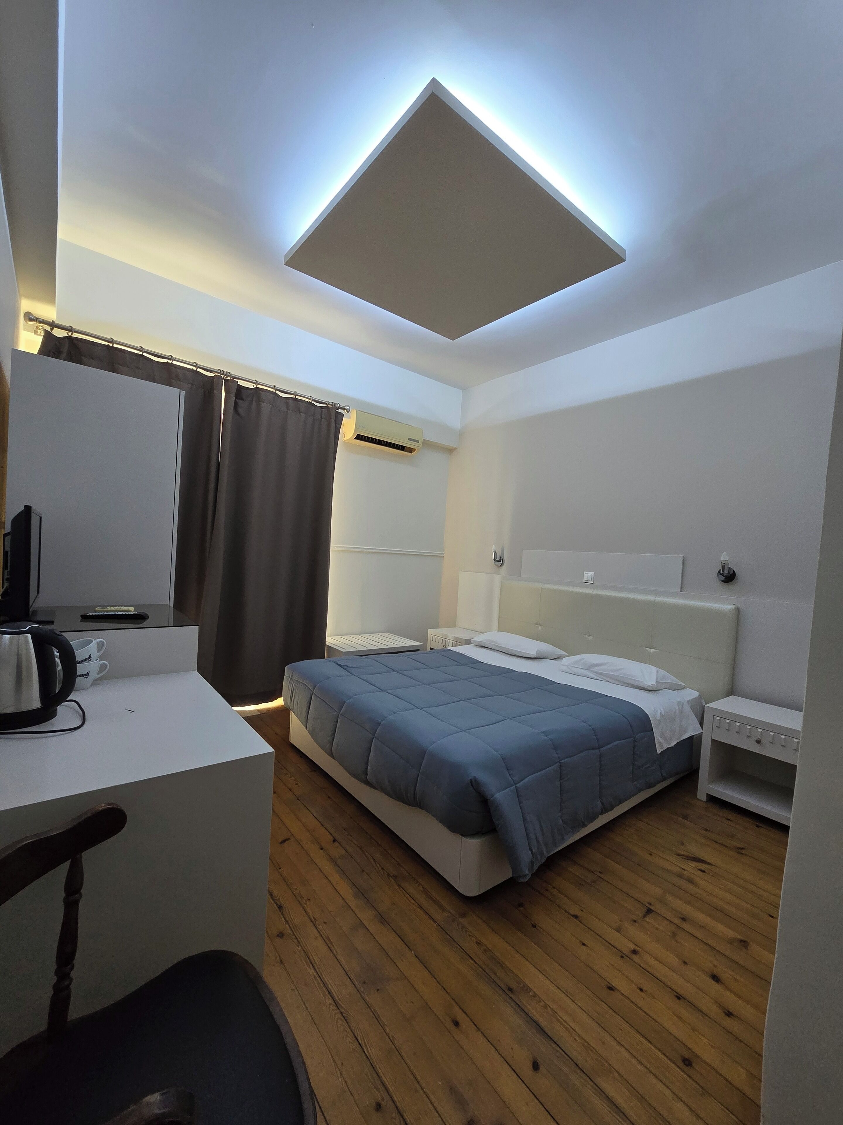 Une chambre d’hôtel moderne équipée d’un lit, d’une table de chevet, d’un bureau, d’une chaise et d’un luminaire au plafond.