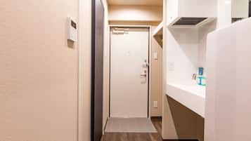 A narrow hallway with a wooden floor, a white door, and a white wall with a thermostat.