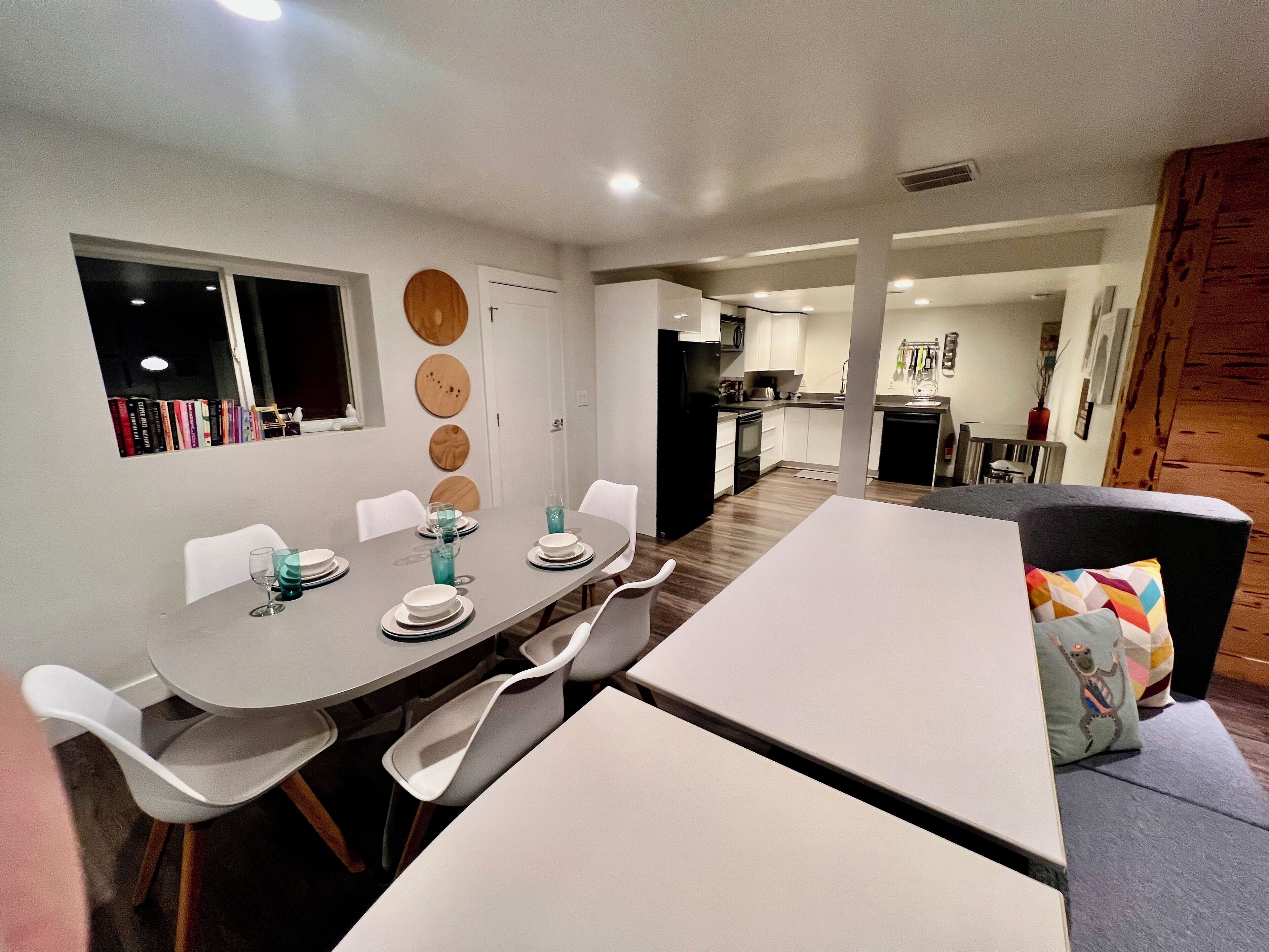 A modern dining area with a round table, white chairs, and a grey sofa.