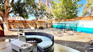 A patio with a curved sofa and a coffee table, surrounded by a wooden fence and trees.
