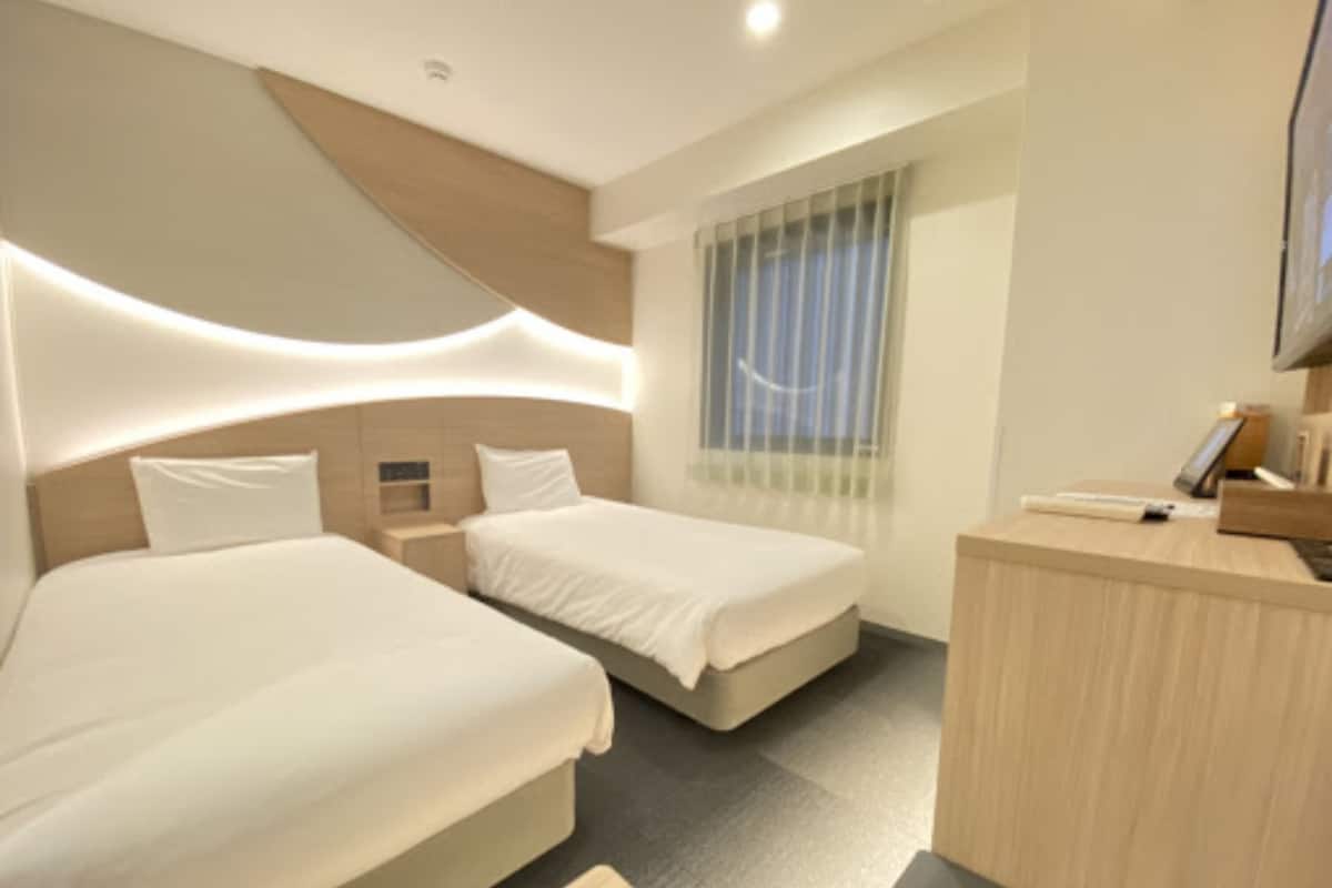 A modern hotel room with two beds, a desk, and a TV.