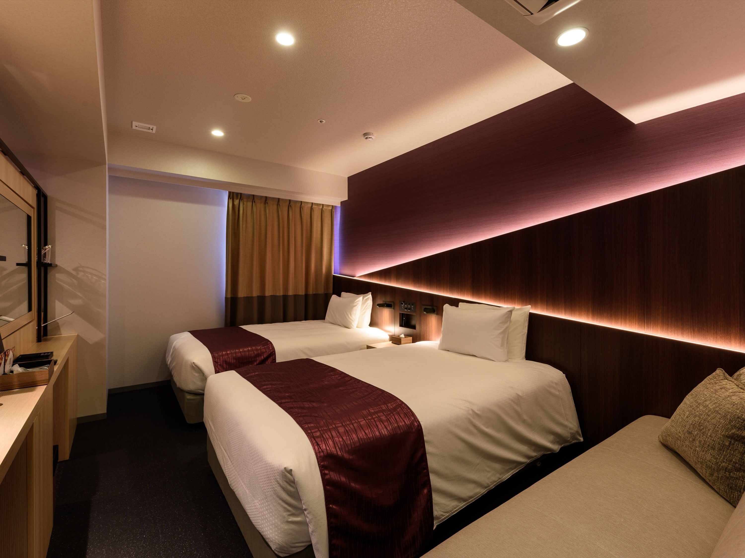 A hotel room with two beds, a desk, and a mirror.