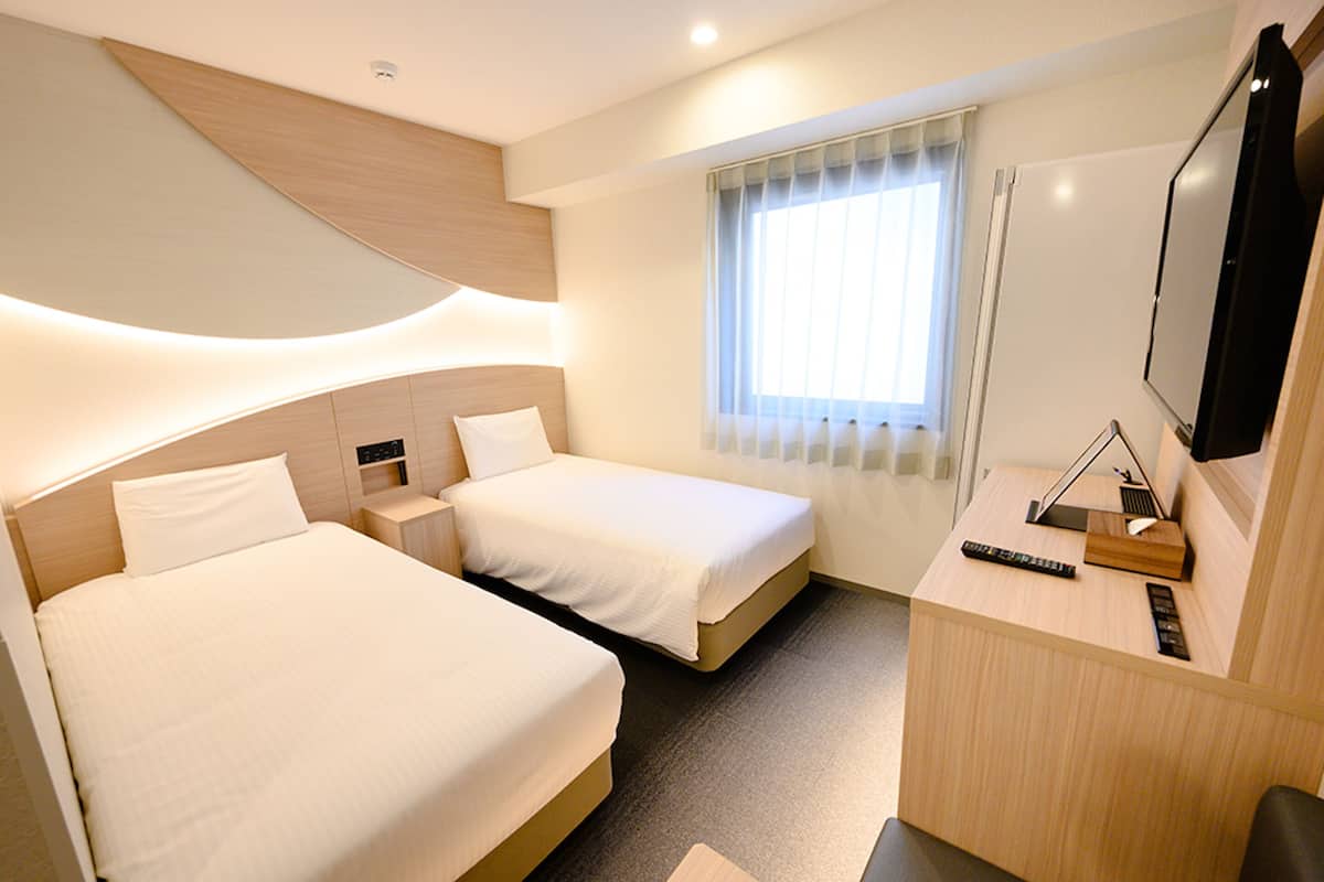 A hotel room with two beds, a desk with a TV, and a window with curtains.