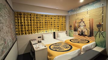 A hotel room with two beds, a desk with a phone and a small table, and a mural on the wall.