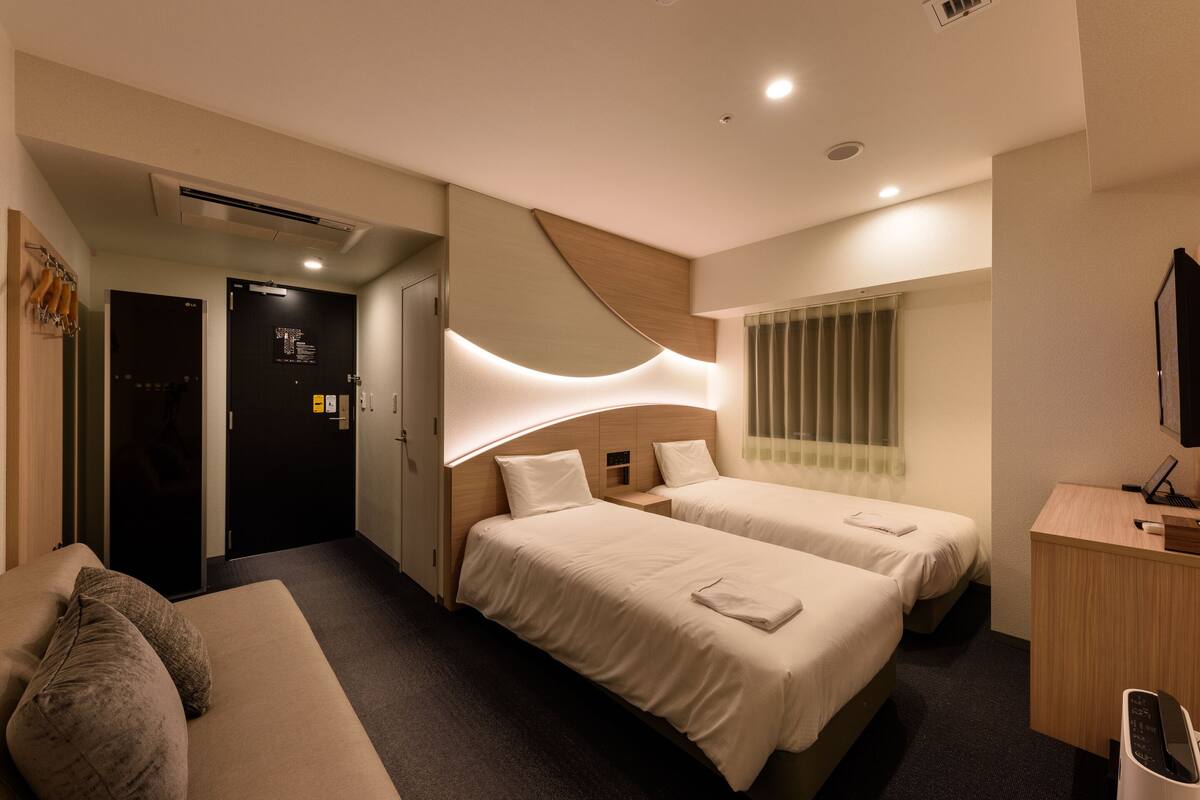 A hotel room with two beds, a desk, a TV, and a sofa.