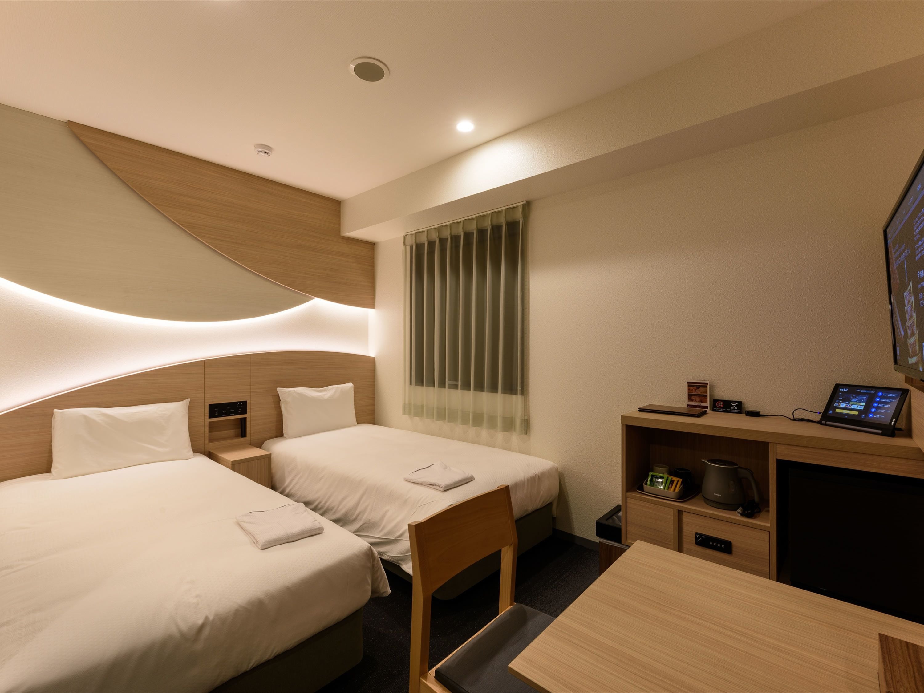 A hotel room with two beds, a desk, a coffee maker, and a TV.