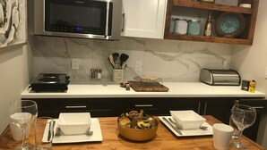 Une cuisine moderne équipée d’un four à micro-ondes encastré, d’un grille-pain et d’une planche à découper en bois. On y trouve des bols, des verres et une bouteille sur le comptoir.