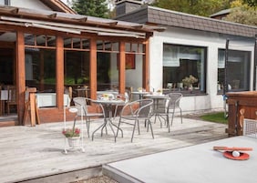 Eine Terrasse im Freien mit Tischen und Stühlen, einer Pergola und Blick auf ein modernes Gebäude.