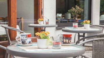 An outdoor seating area with round tables, some with potted plants and coffee mugs.