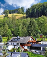 Ein modernes Haus mit großzügigem Balkon, umgeben von üppiger Vegetation und einer hügeligen Landschaft.