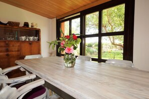Enjoy meals in this dining area with a long table and comfortable seating for four, surrounded by a view of lush greenery.