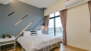 Une chambre moderne avec un lit, une table de chevet et une vue sur la ville grâce à de grandes fenêtres.