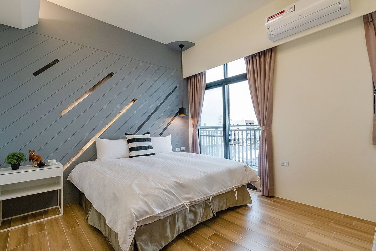 Un dormitorio moderno con cama, mesita de noche y vistas a la ciudad a través de amplios ventanales.