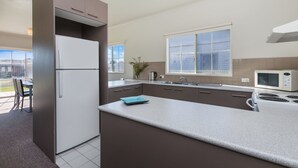 A modern kitchen with a refrigerator, stove, microwave, and a large window providing natural light. - Julieanne (Port Fairy)