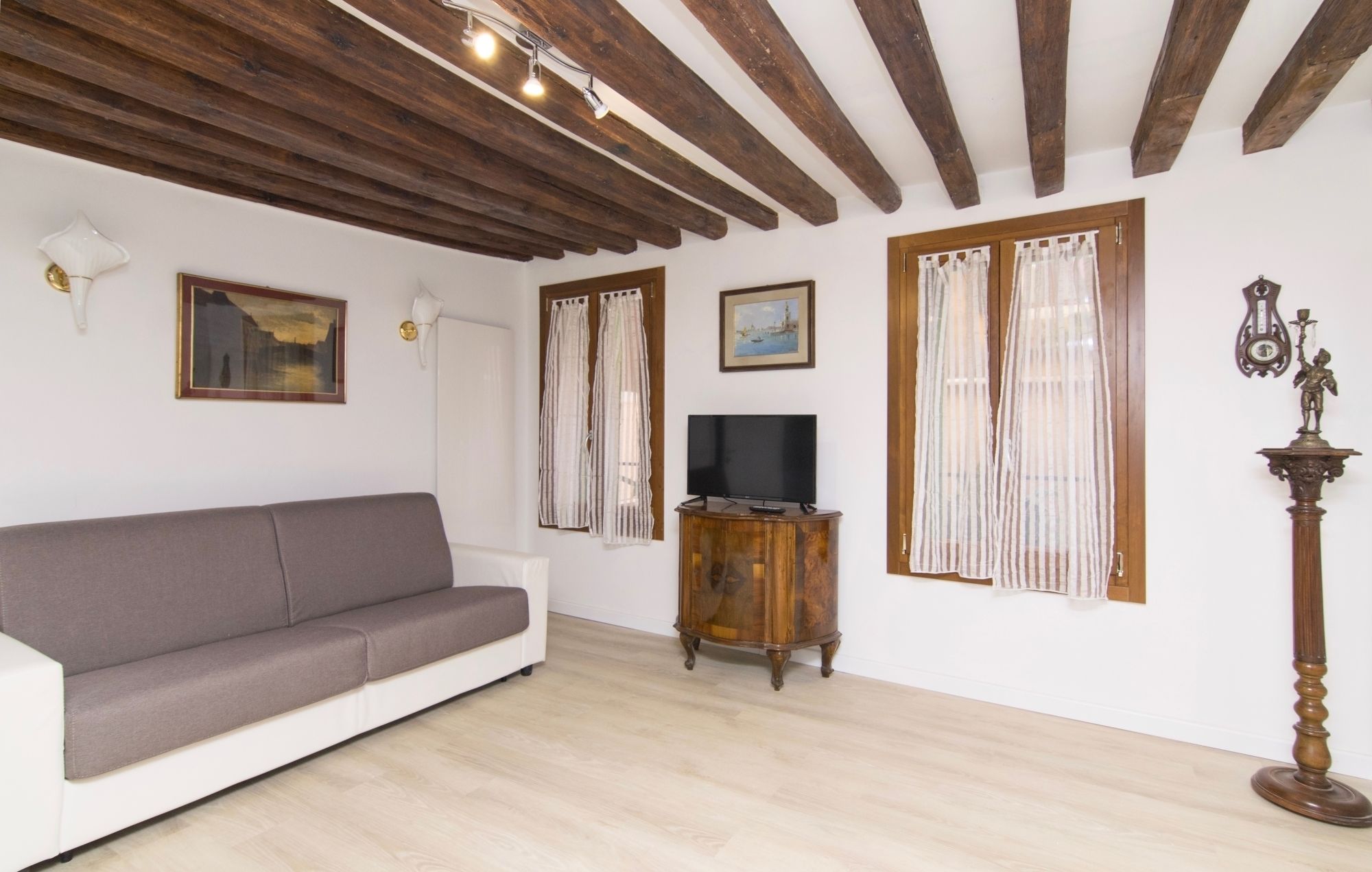 Uma sala de estar com sofá cinza, piso de madeira e uma TV sobre suporte de madeira.
