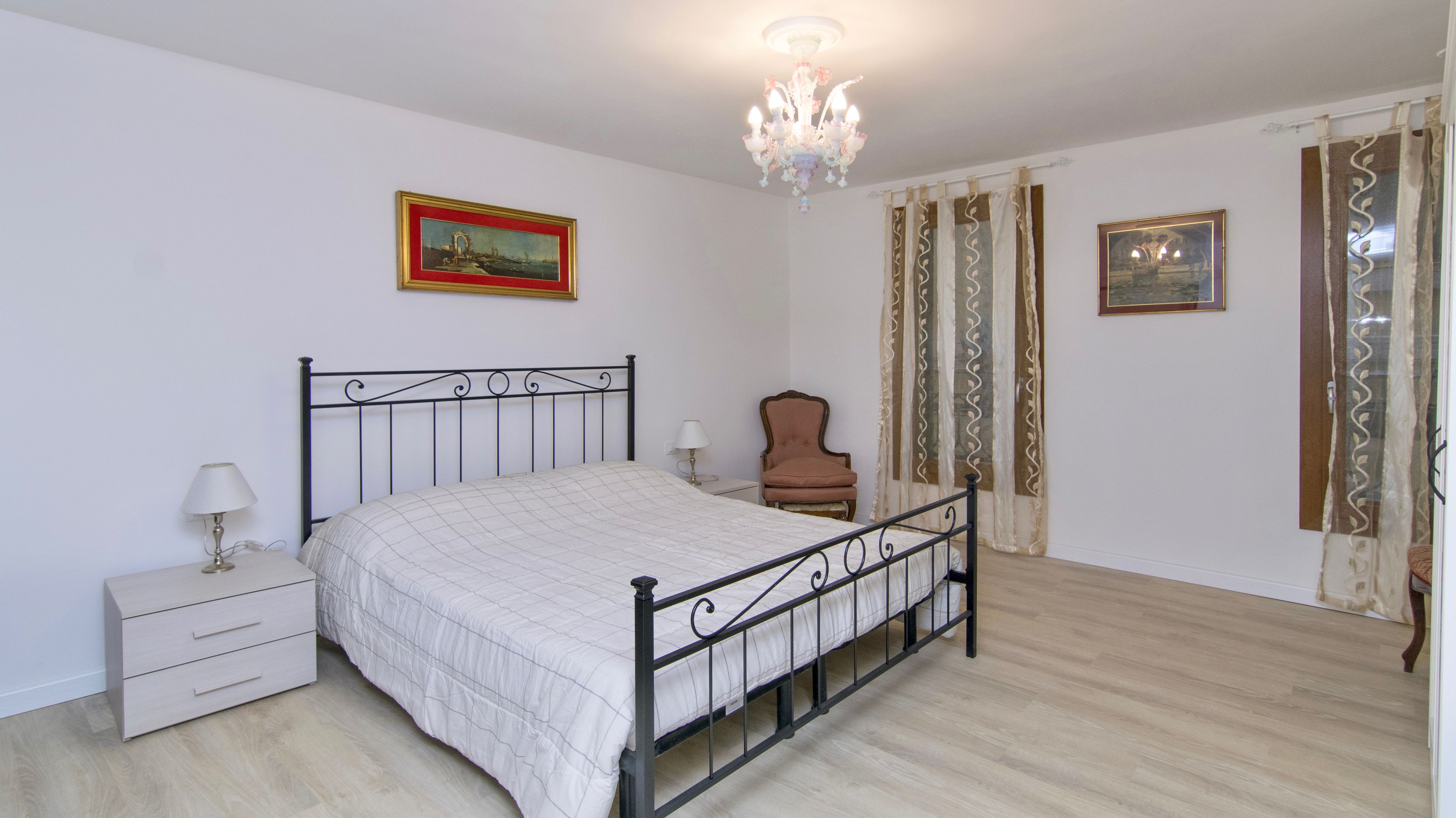 Une chambre à coucher comprenant un lit, une table de chevet, une chaise, un lustre et deux tableaux encadrés accrochés au mur.