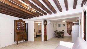 A spacious living area with a wooden ceiling, a large cabinet, a dining table with chairs, and a white sofa. - Ca' Alberto Apartments 1 (Venice)